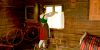 Kansallispukuinen nainen ripustaa verhoa ikkunaan vanhassa hirsitalossa. Huoneessa on myös rukkeja ja sänky.. Kuvaaja: Hannu Lindroos
